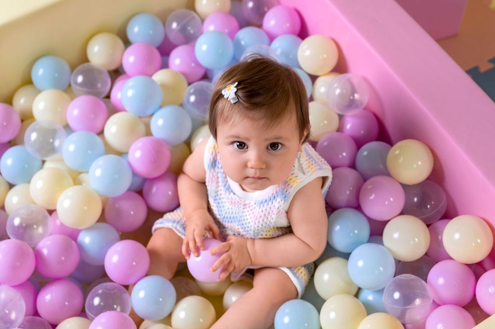 Baby plays among colorful pastel blue, pink and white ball pit balls in soft lighting.