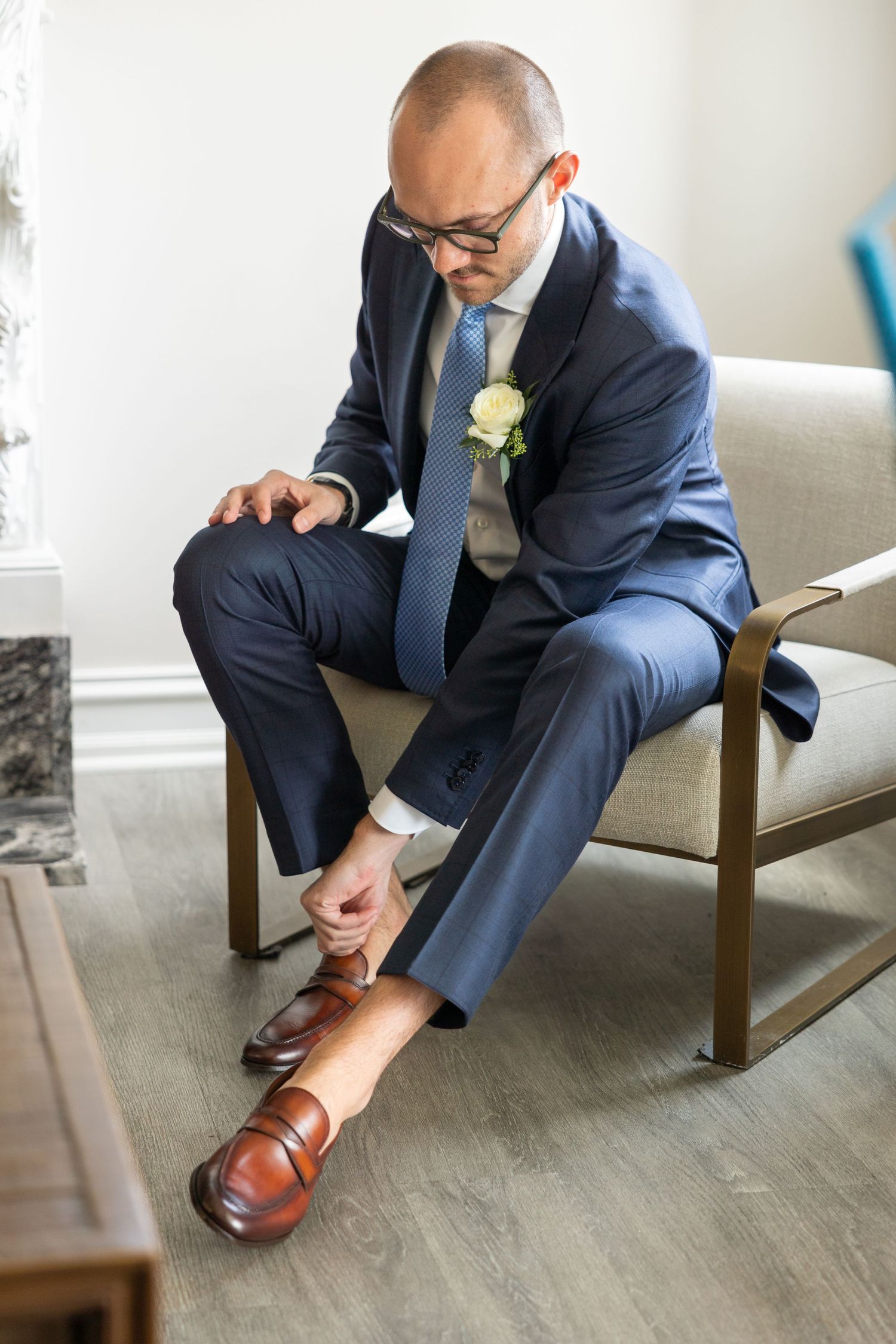 Getting dressed in a navy suit and adjusting brown leather dress shoes while wearing a boutonniere. Rachel Martinez Photography