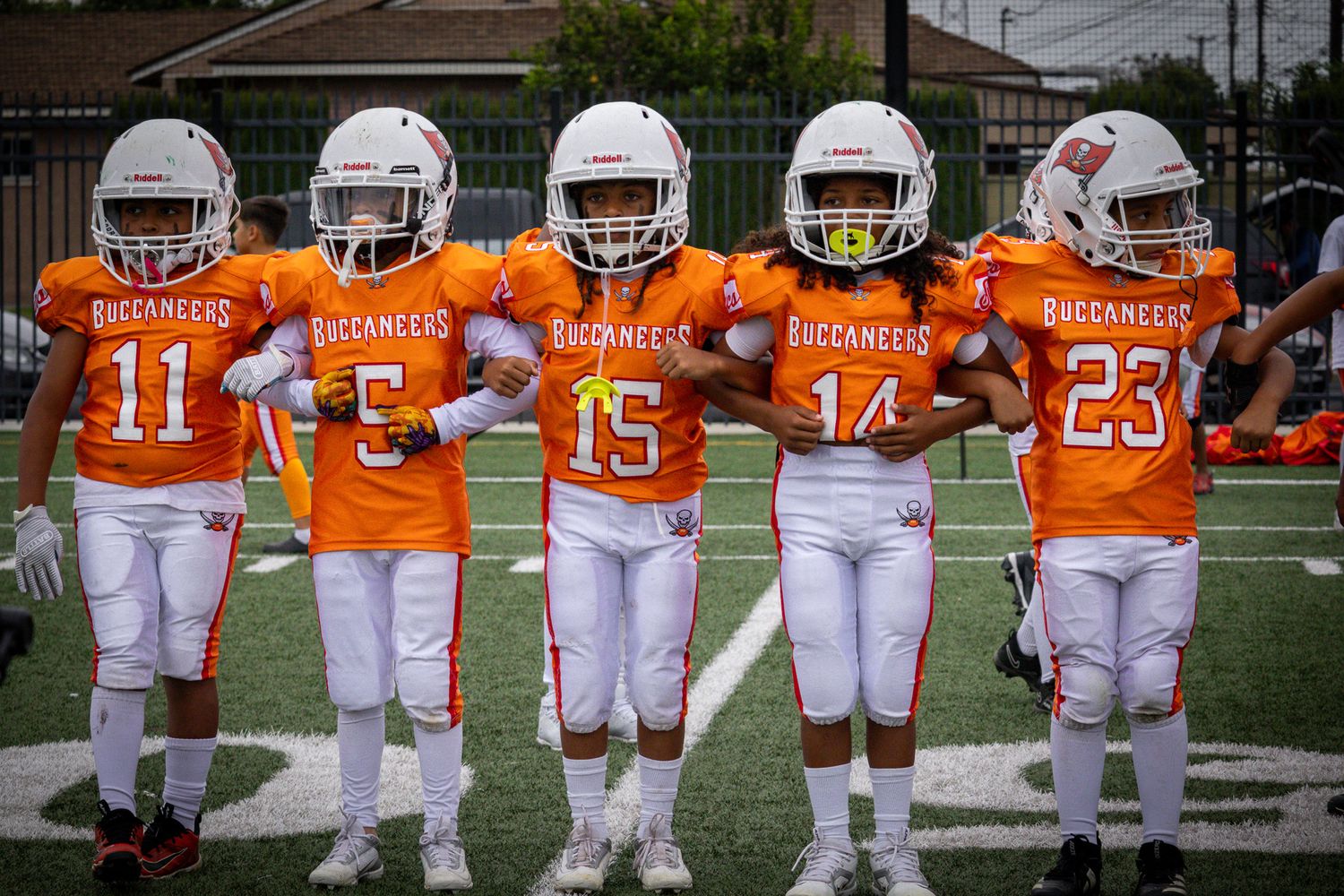 Youth football team lines up in orange and white uniforms on a playing field.