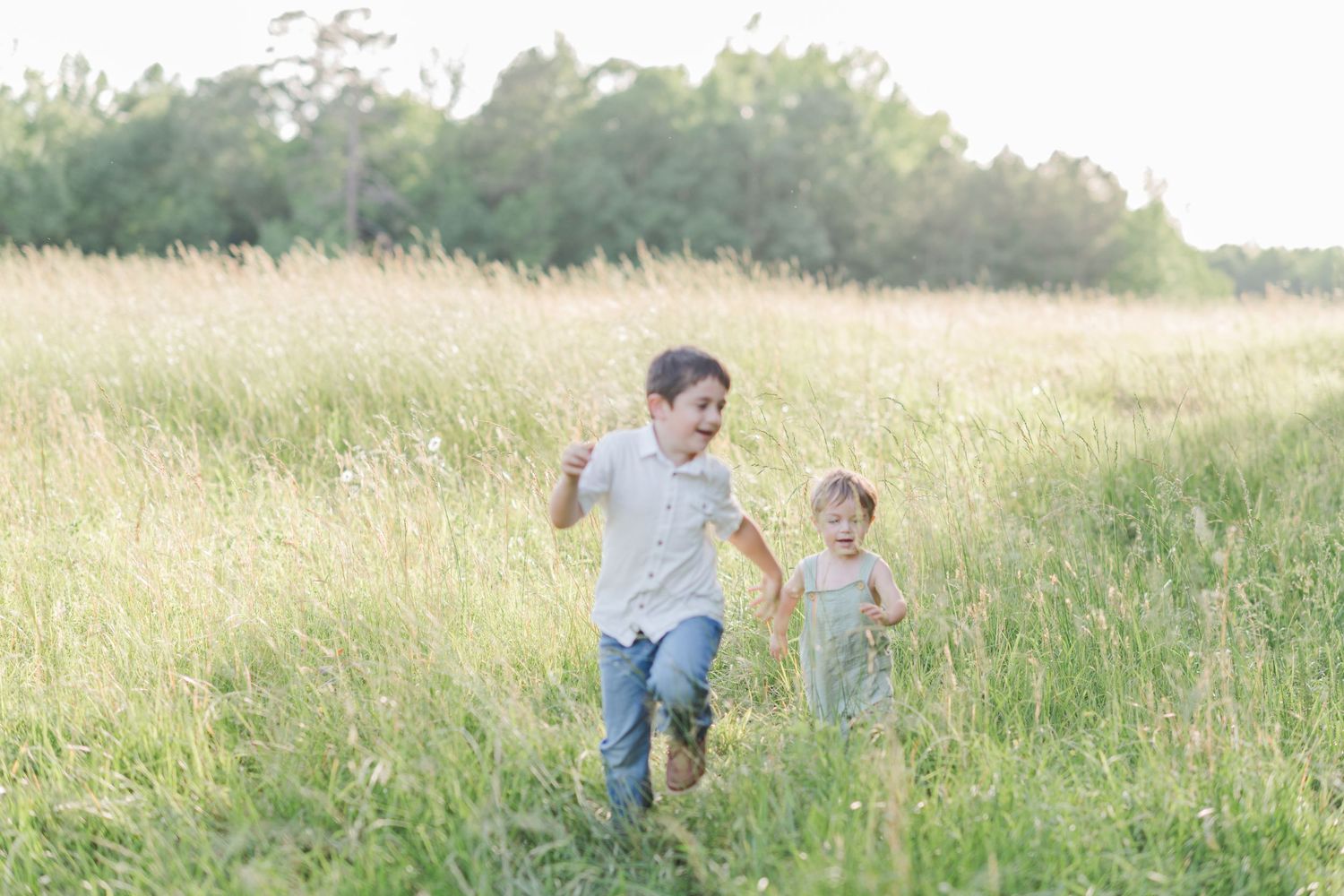 Two children running and laughing through a tall grass meadow in golden sunlight.