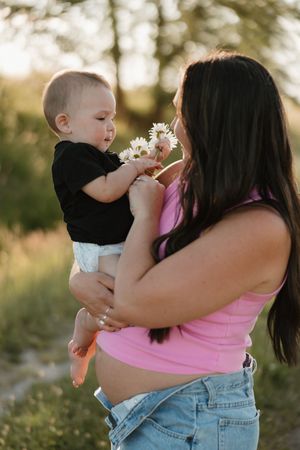 Parent and baby sharing a tender moment outdoors while looking at a dandelion flower together in golden sunlight.