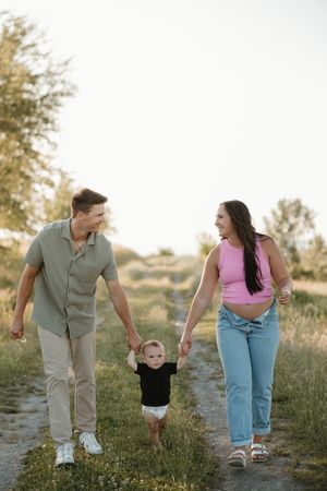 A young family walks hand in hand along a dirt path through a field during golden hour.
