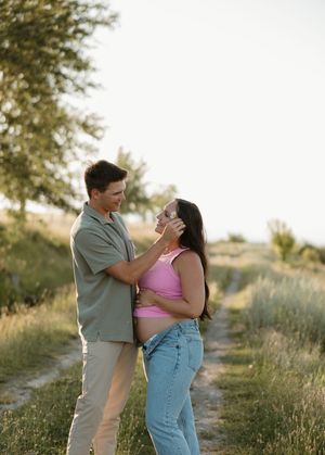 Romantic couple sharing an intimate moment together on a dirt path surrounded by nature at sunset.