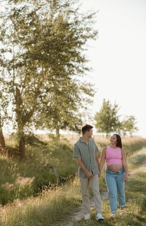 Couple walking hand in hand along a scenic nature path during golden hour with trees in the background.