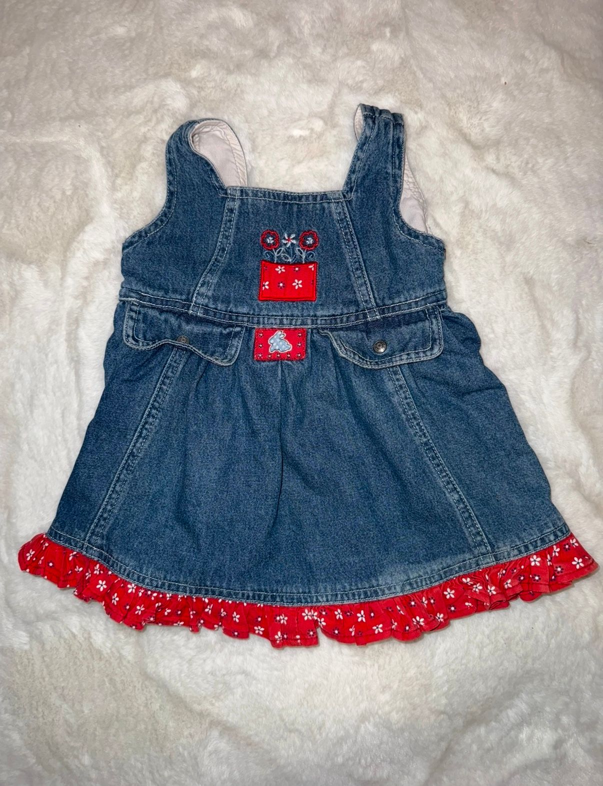 Denim baby dress with red polka dot trim and castle applique laid flat on white surface.