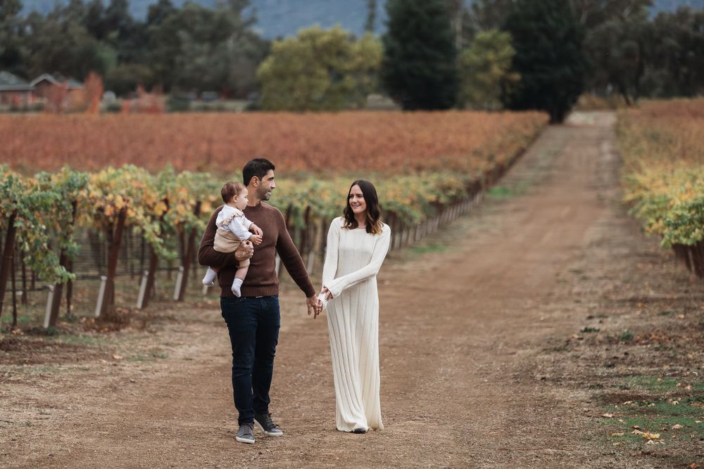 Two people walking together on a dirt path between autumn vineyard rows under overcast skies.