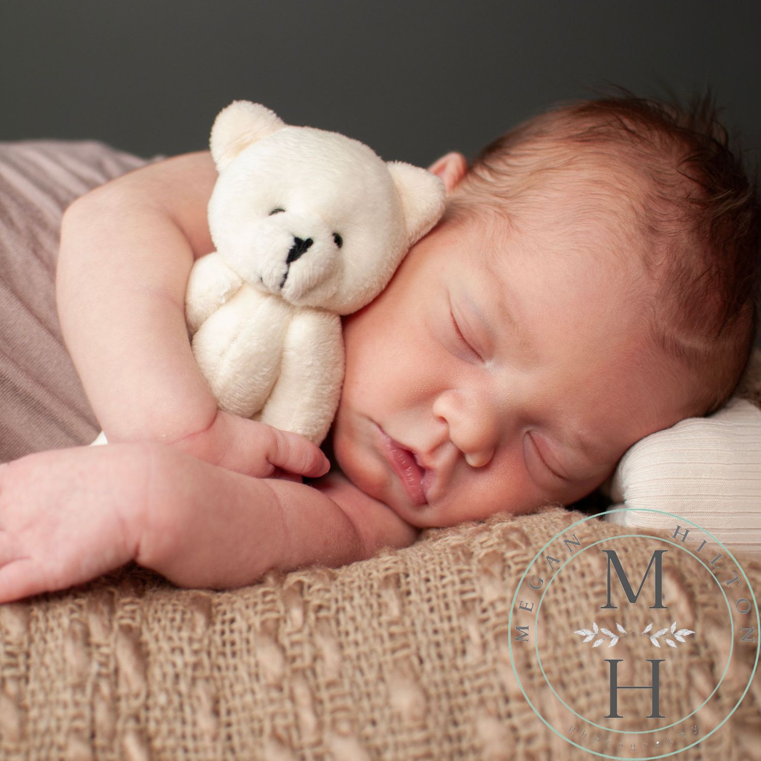 Peaceful sleeping baby cuddling with small white teddy bear on textured burlap backdrop.