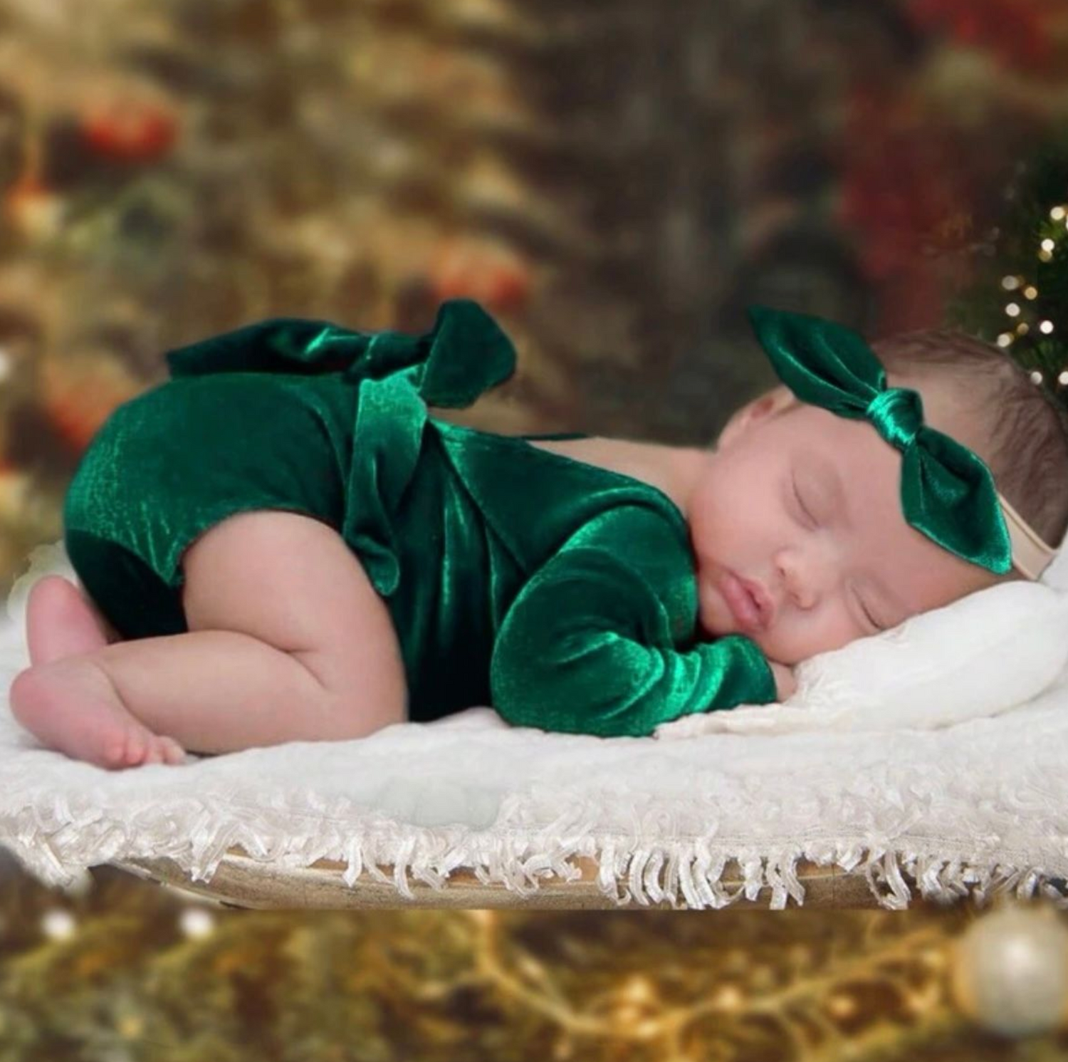Newborn wearing emerald green outfit sleeping on white textured blanket.