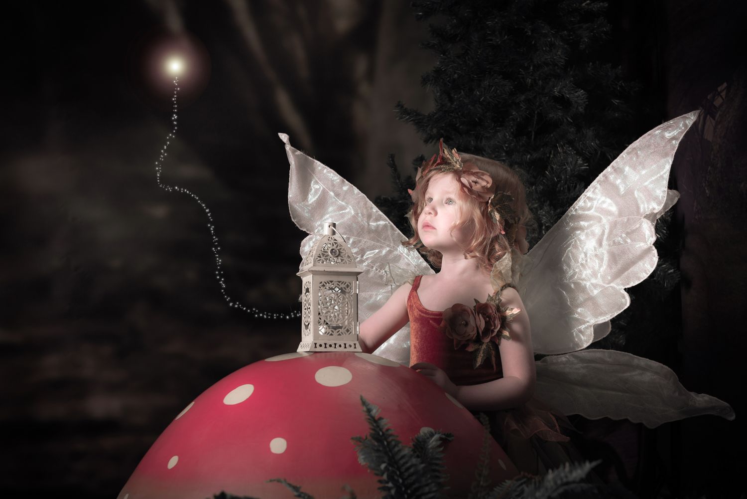 A fairy perches atop a red spotted mushroom beneath magical twinkling lights in a dark forest.