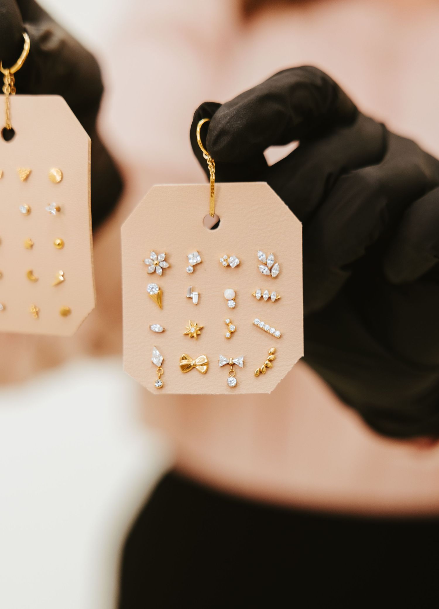 Black gloved hands displaying a card with gold and silver earring designs.