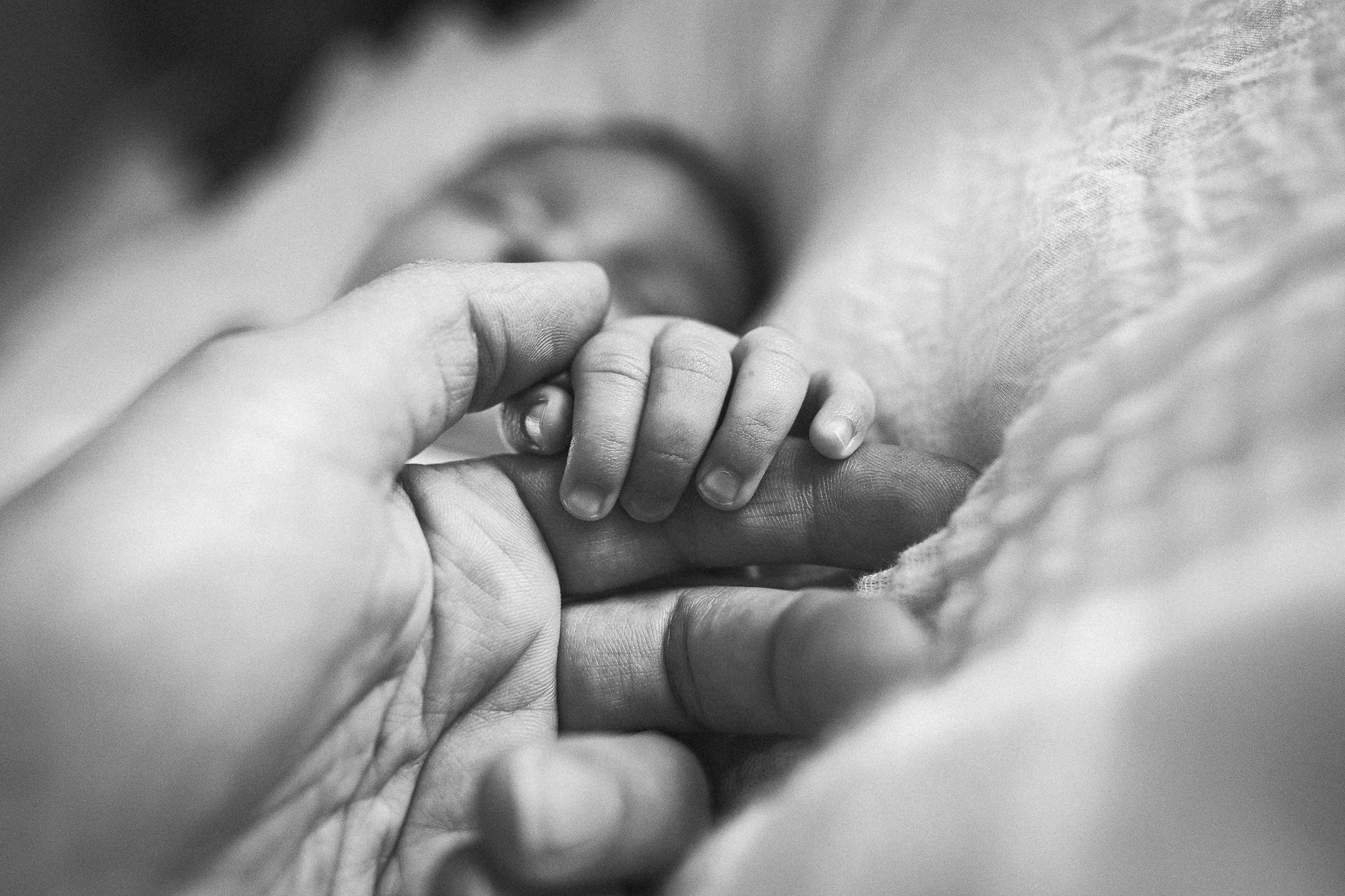 A black and white close-up of a newborn baby grasping a parent's finger tenderly.