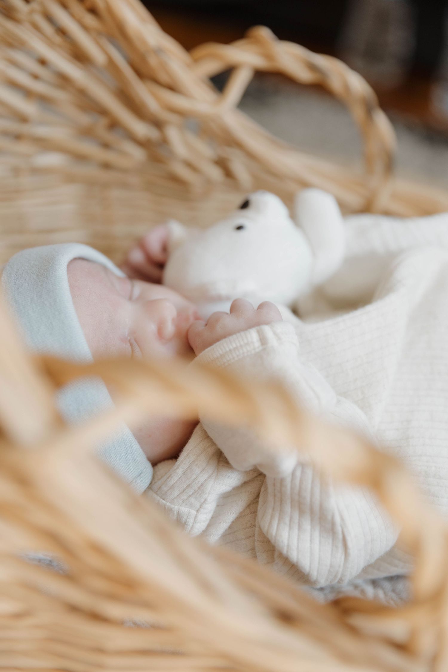 A soft white stuffed toy bunny rests in a woven wicker basket with delicate white fabric.