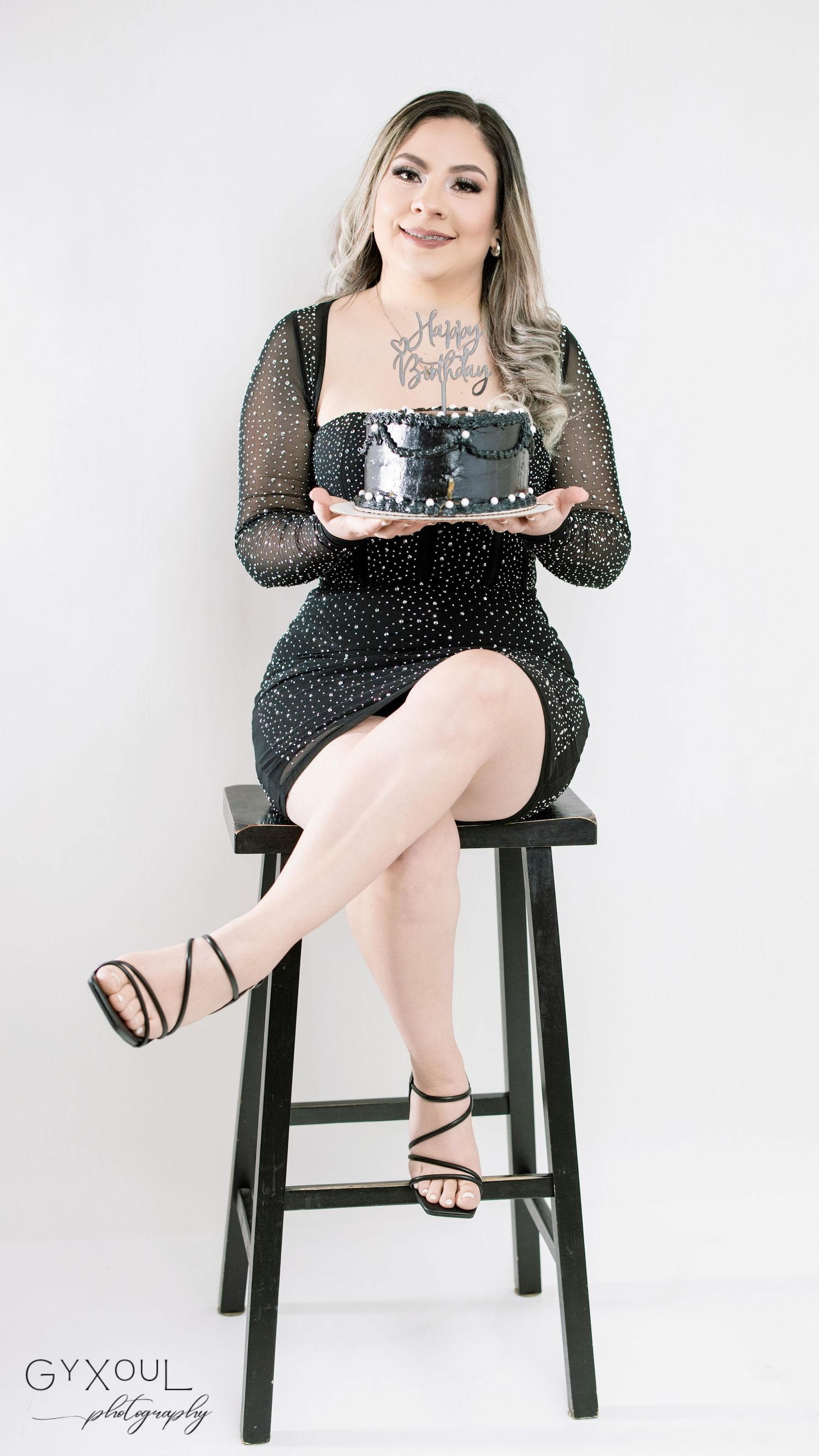 Sparkling black dress portrait on wooden stool with decorative cake.