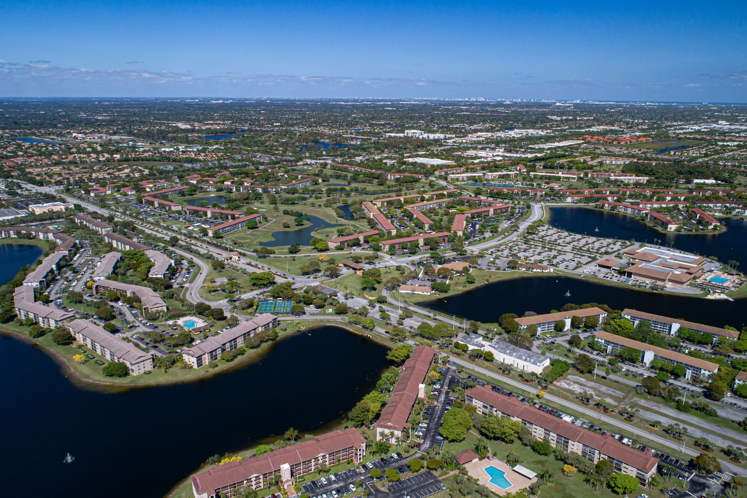 Aerial view of suburban neighborhood showing rows of terracotta-roofed houses with swimming pools and palm trees in Florida.