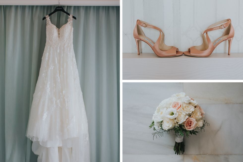 A white lace wedding dress hangs beside tan strappy heels and a blush and white rose bridal bouquet.