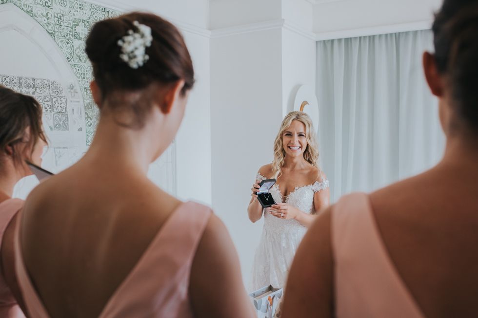 An elegant bridal party moment as they admire their reflections in a bright white room with soft decor.