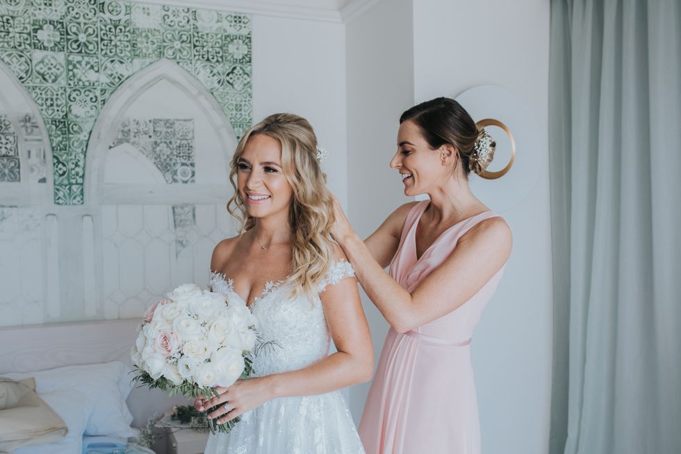 Wedding preparation scene with white bridal bouquet and soft pink bridesmaid dress in an elegant room setting.