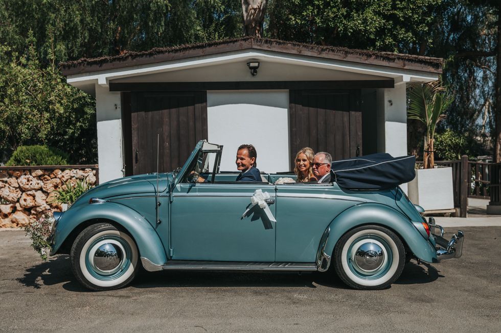 A classic turquoise Volkswagen Beetle convertible with white wall tires parked in front of a white garage.