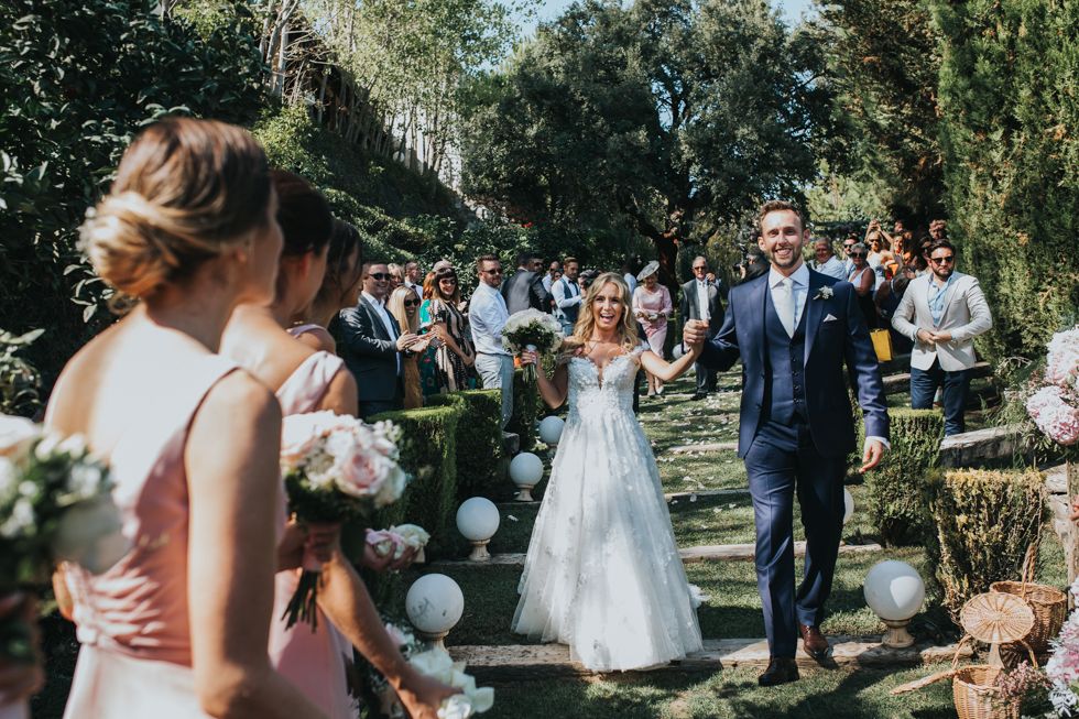 Sunny outdoor garden wedding celebration with white balloons lining the pathway amongst lush greenery.