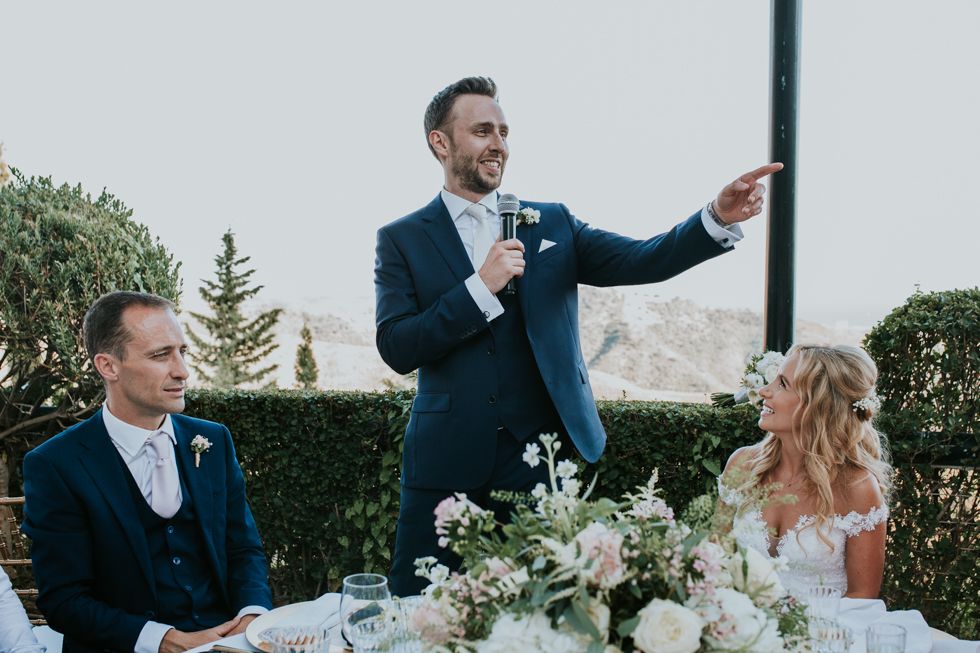 Wedding speech being delivered at an outdoor reception with elegant floral centerpieces and table settings.