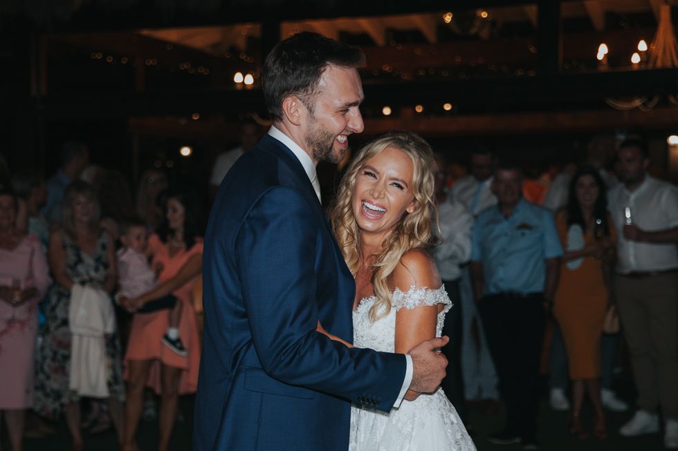 A happy couple share a joyful dance moment at their wedding reception with guests in the background.