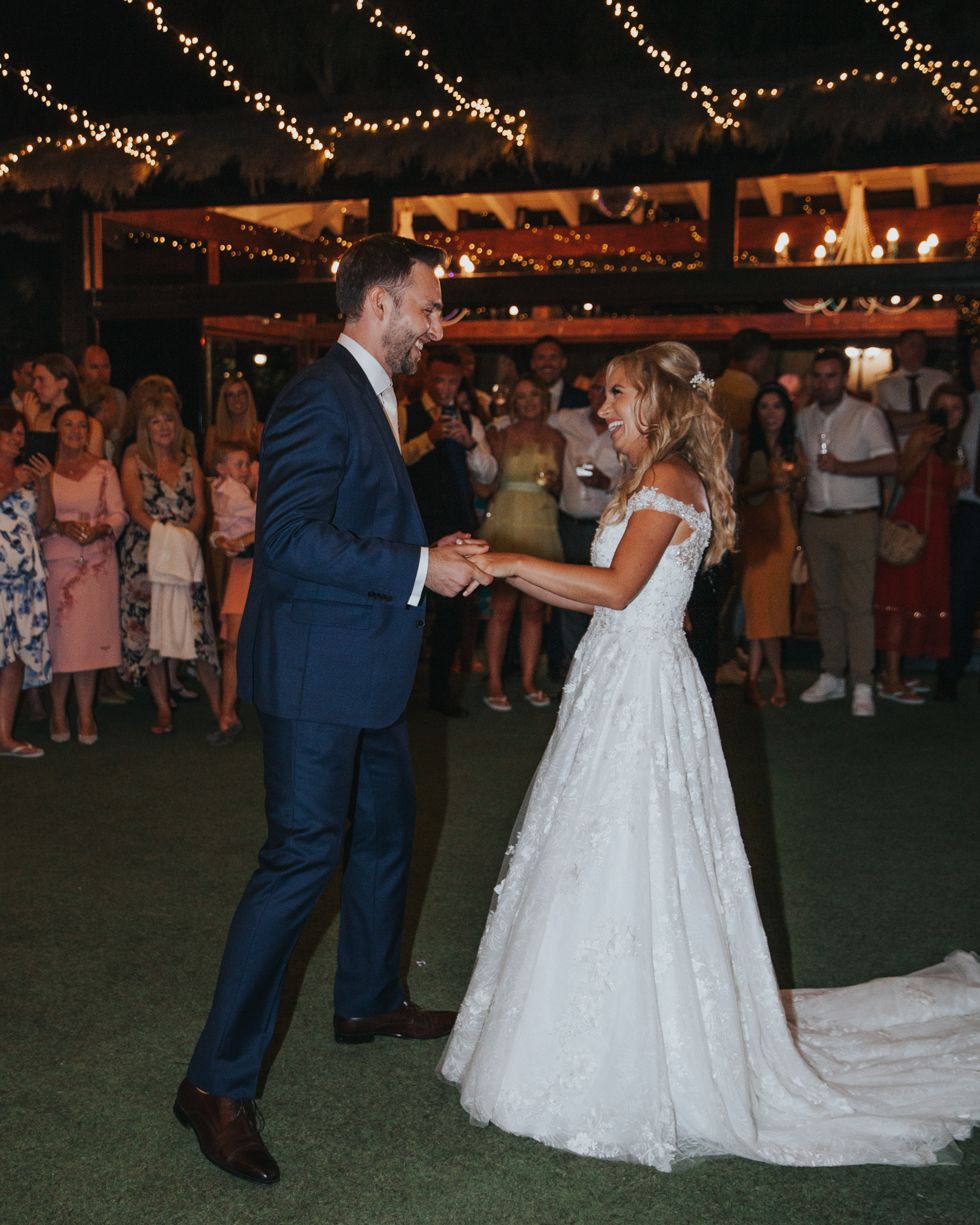 A couple shares their first dance at an outdoor evening wedding reception under twinkling string lights.