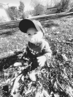 Black and white photo of baby playing in fallen leaves during autumn.