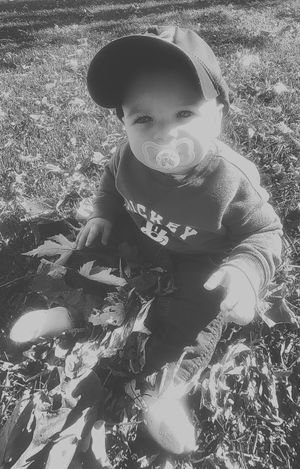 Baby wearing baseball cap and pacifier plays in scattered autumn leaves.