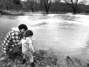 People examining the edge of flooded waters near a riverbank.