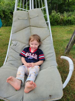 A child relaxes in a white outdoor hammock chair on a sunny day.