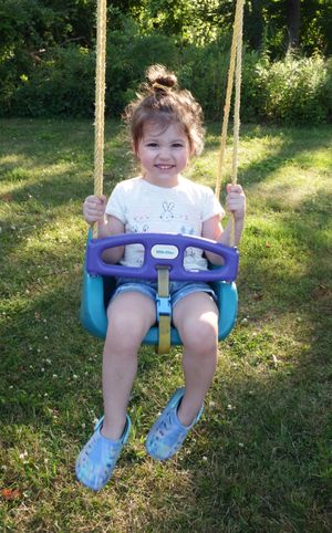 Child enjoying a blue and purple outdoor swing set on a sunny summer day.
