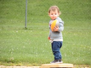 Small child running on grass while holding an orange ball.