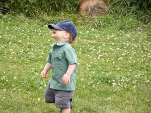 Child walking across grassy field wearing casual summer clothes.