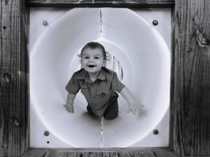 A series of black and white photos showing a child playing in a white tunnel structure.
