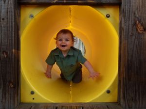 A sequence of photos showing a child playing inside a yellow tunnel playground equipment.