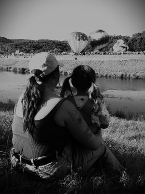 People watching colorful hot air balloons at a lakeside festival in black and white.