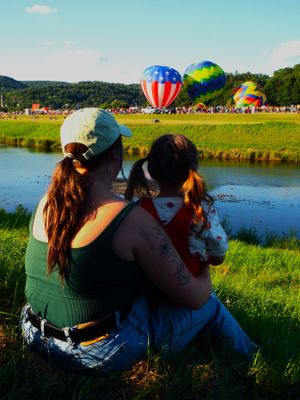 Spectators enjoying a hot air balloon festival by a serene lake on a sunny day.