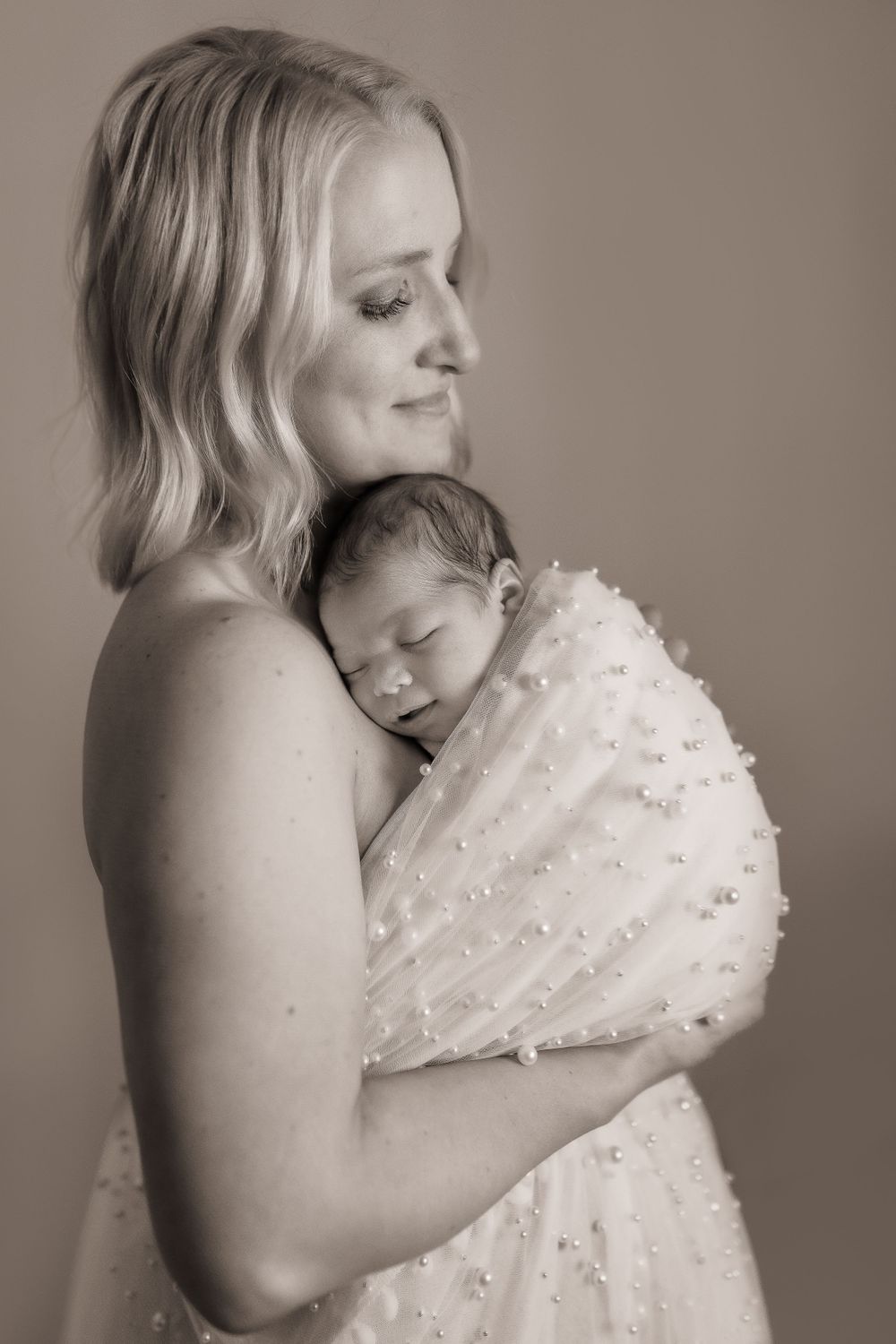 Black and white portrait of tender moment between mother and sleeping newborn in textured dress.