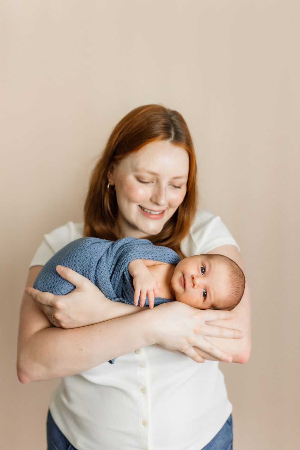 A tender moment between parent and baby as they embrace against a neutral beige background.
