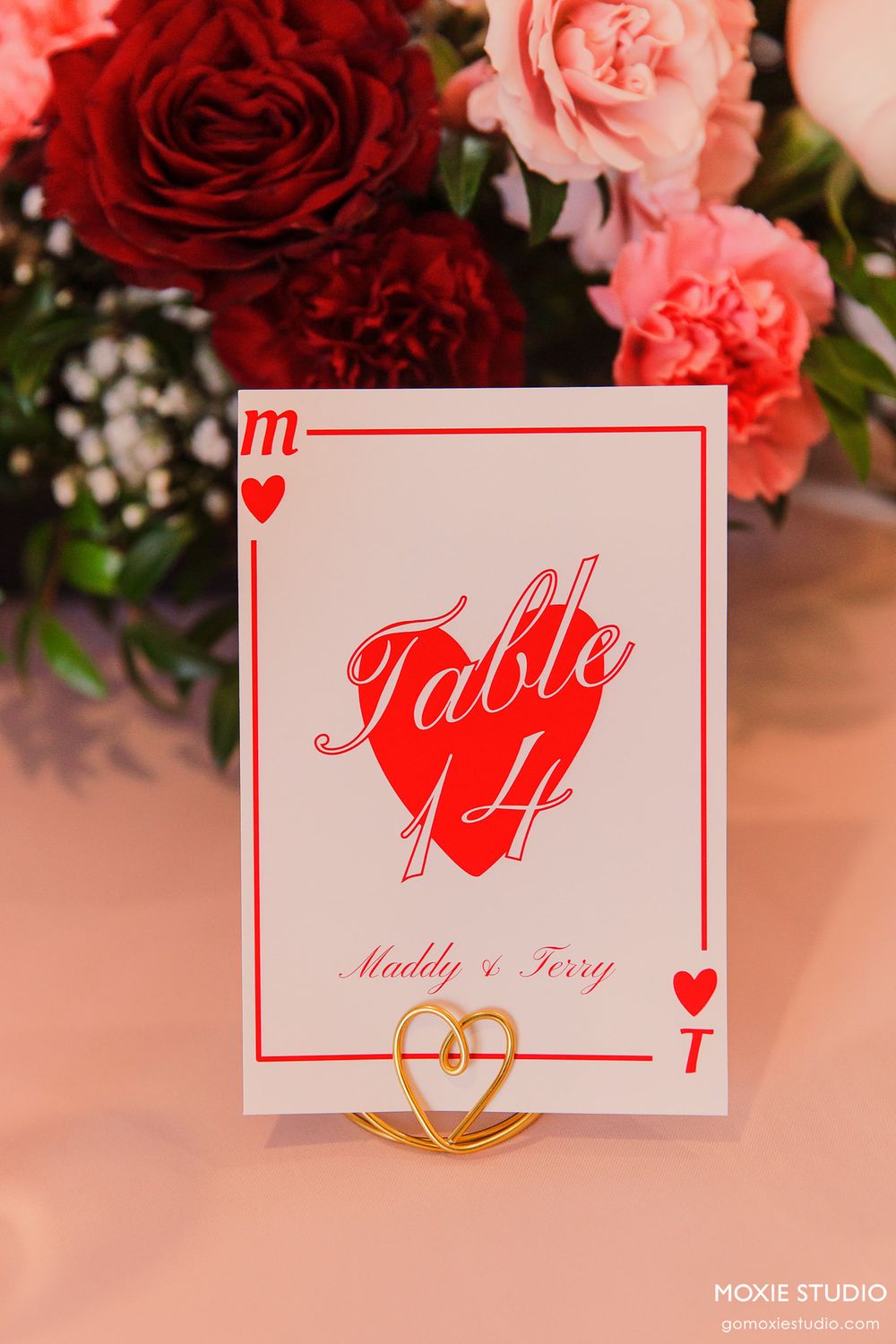 Wedding place cards and decorations featuring red hearts and gold rings among pink and red roses.