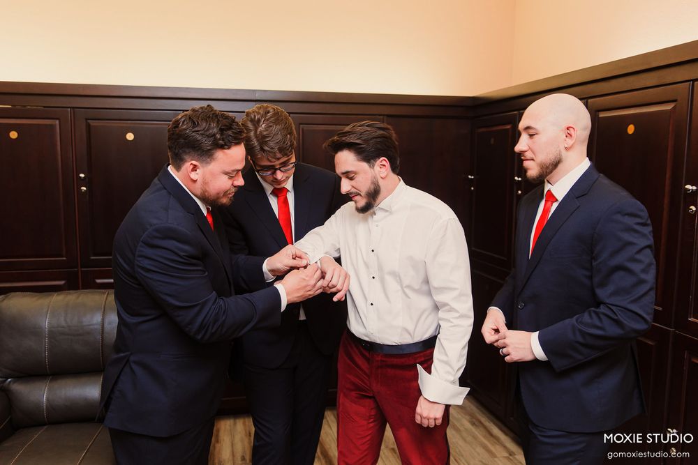 Groomsmen in navy suits and red ties gathered in a room before the ceremony.
