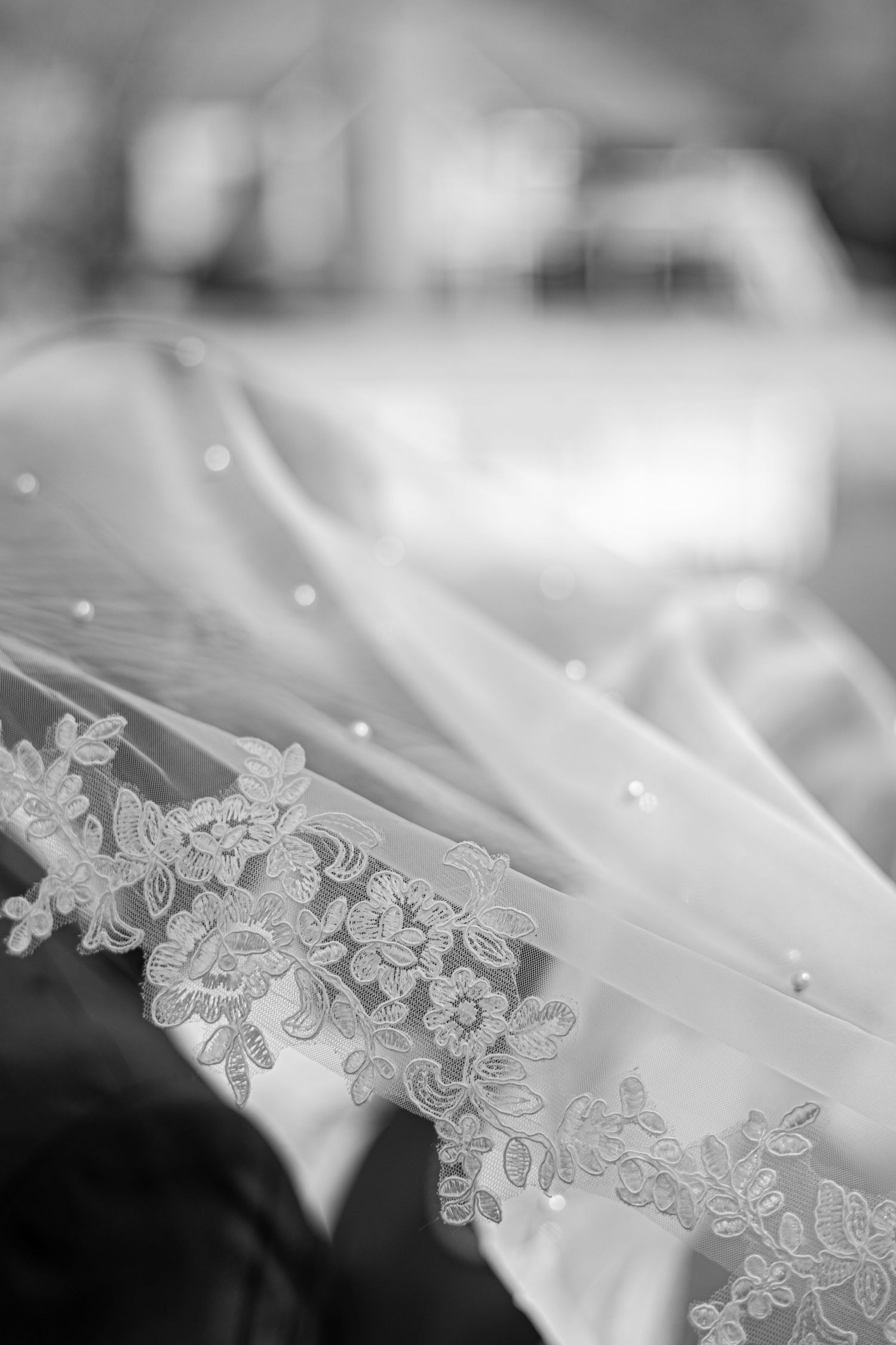 Close-up detail of delicate lace trim on white wedding veil with sparkling embellishments.