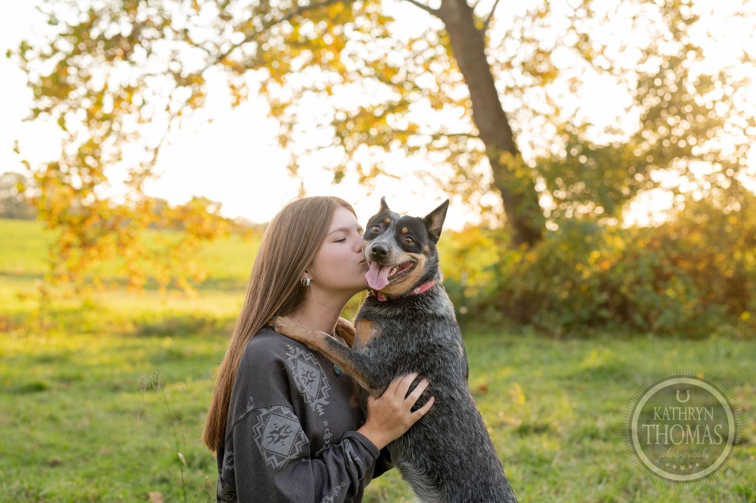 A German Shepherd dog shares an affectionate moment with someone in a fall setting at sunset.