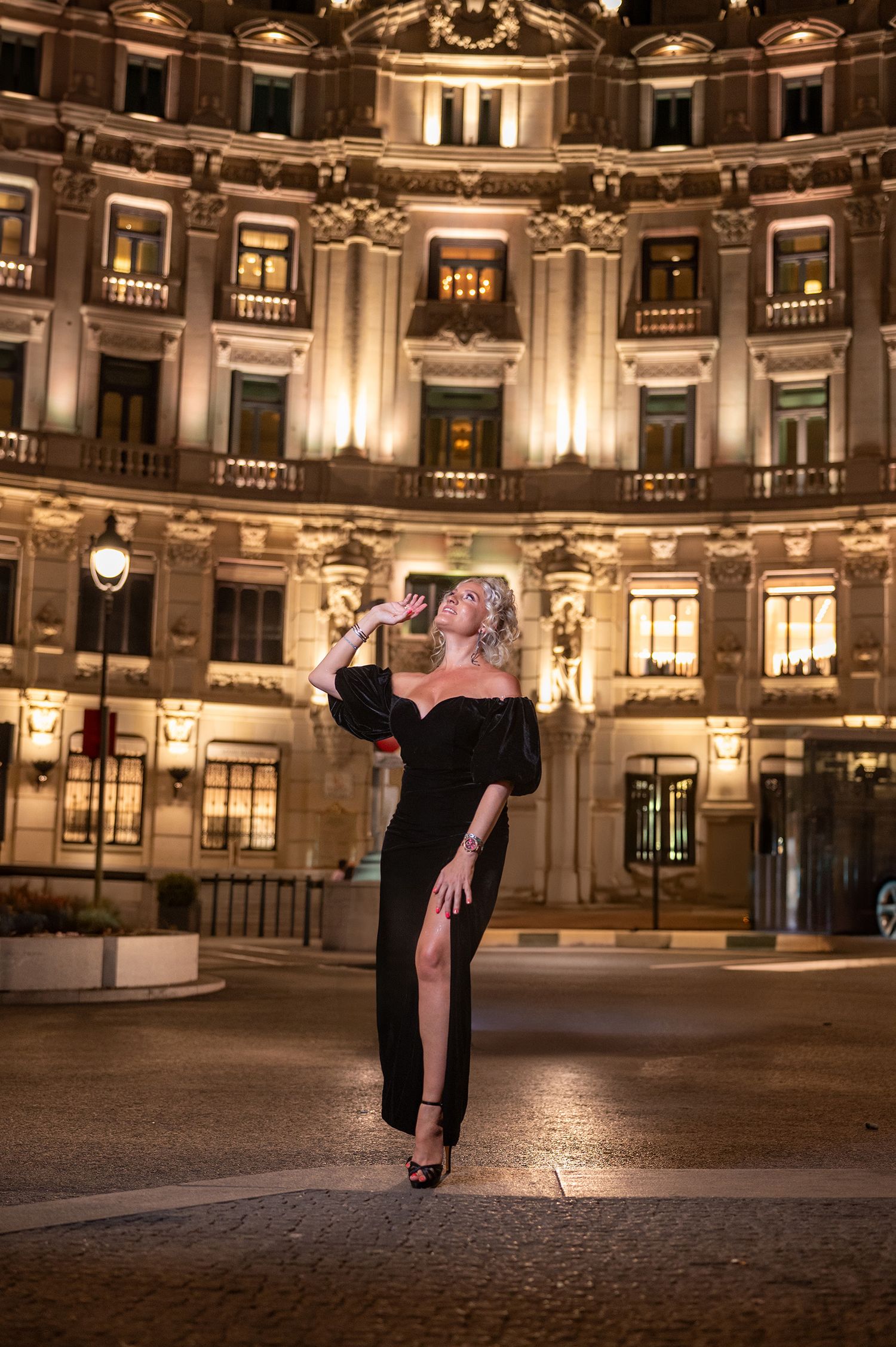 Elegant black evening gown silhouetted against illuminated classical building facade at night.