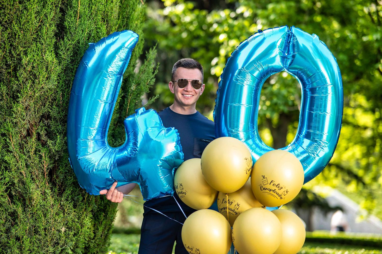 Bright metallic blue number 40 balloons and yellow celebration balloons displayed outdoors against green foliage.