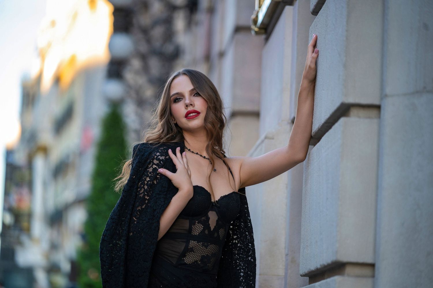A figure in a black sequined outfit poses dramatically against a building exterior in evening light.