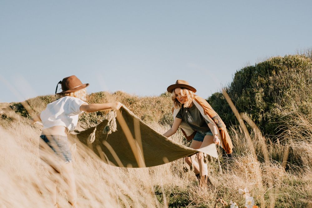 Two people playing with white fabric in golden grass on sunny hillside.
