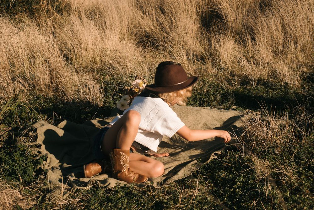 Figure in hat reading book while lounging in sun-dried grass.
