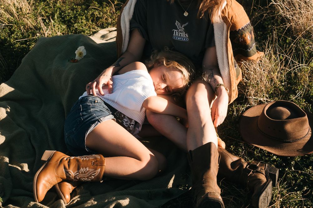 Person resting on blanket outdoors with brown boots and ceramic pot nearby.