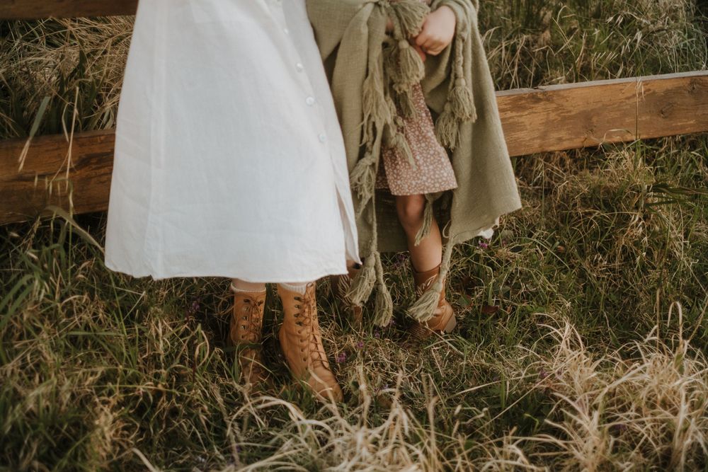 Cropped view of vintage boots and dresses against wooden fence in field.